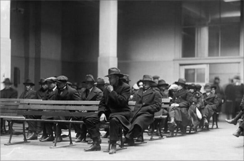 Men in overcoats and hats sit on rows of benches.